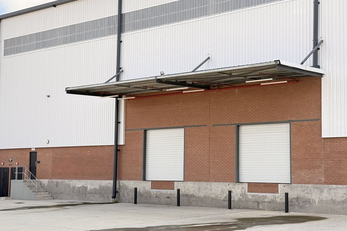 Industrial warehouse exterior featuring two roller shutter loading doors, a protective canopy, and a concrete loading apron with bollards.