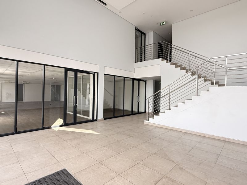 Spacious modern industrial entrance foyer featuring a prominent staircase with stainless steel balustrades, large glass partitions, and clean tiled flooring.