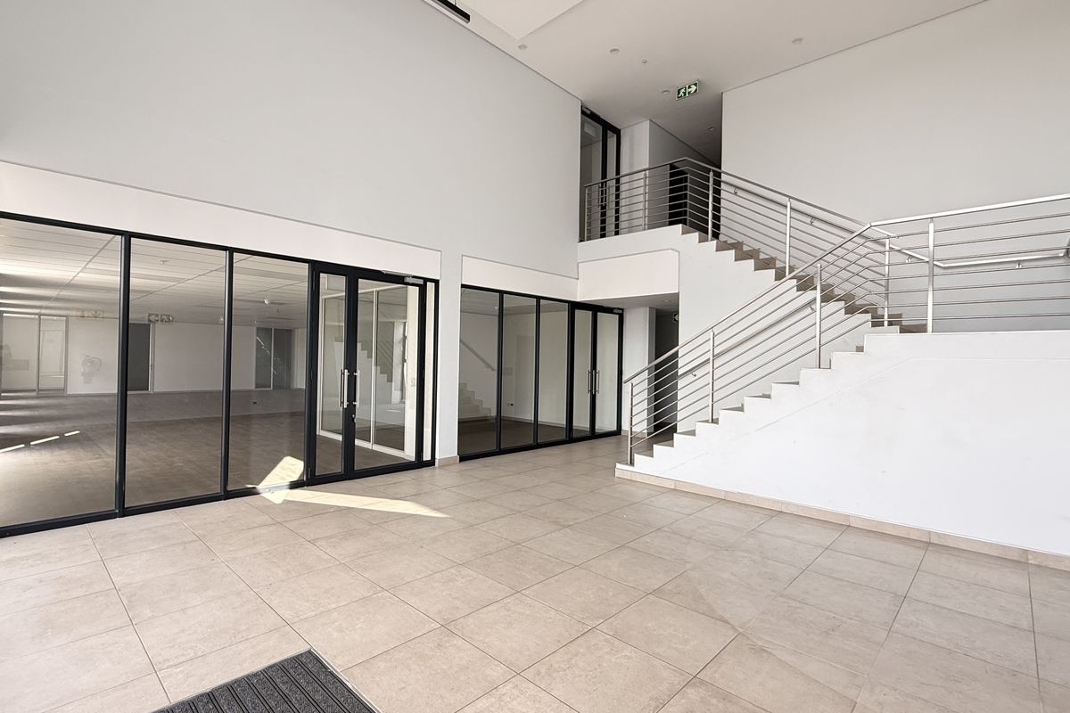 Spacious modern industrial entrance foyer featuring a prominent staircase with stainless steel balustrades, large glass partitions, and clean tiled flooring.