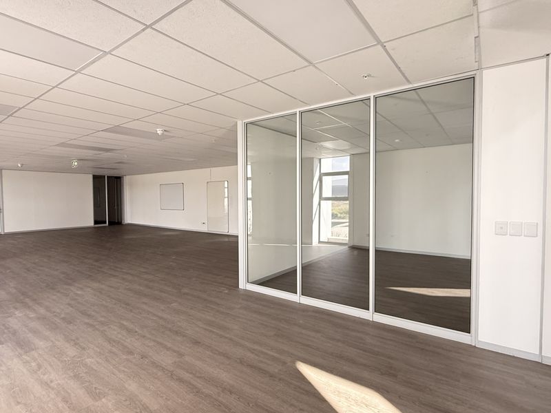 Spacious open-plan office area featuring modern glass partitions, suspended ceilings, and durable laminate flooring, offering a clean and professional workspace environment.