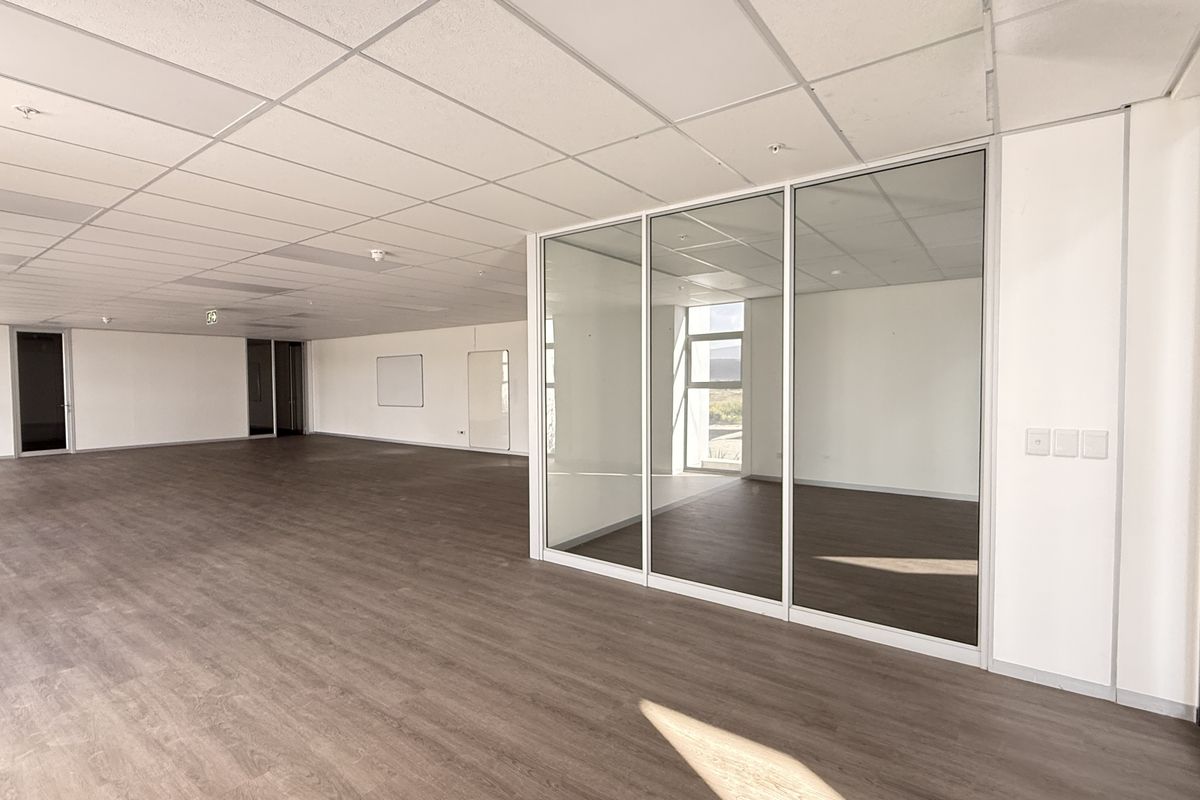Spacious open-plan office area featuring modern glass partitions, suspended ceilings, and durable laminate flooring, offering a clean and professional workspace environment.