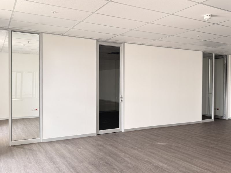 A bright, vacant office space featuring modern glass partitions, suspended ceilings, and durable laminate flooring, suitable for a professional workspace layout.
