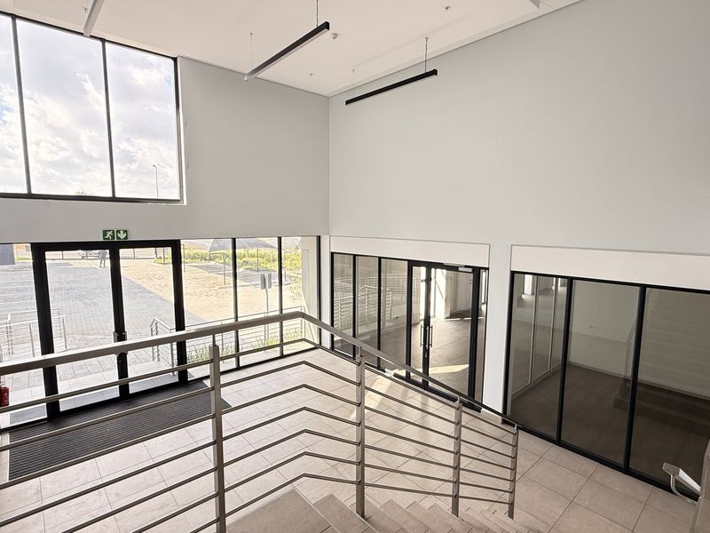 Modern industrial entrance foyer featuring high ceilings, large glass windows, tiled flooring, and a stainless steel staircase balustrade.