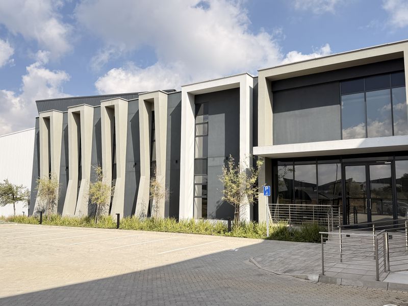 Modern industrial building facade featuring architectural fins, large glass windows, and a paved parking area with accessible ramp access.