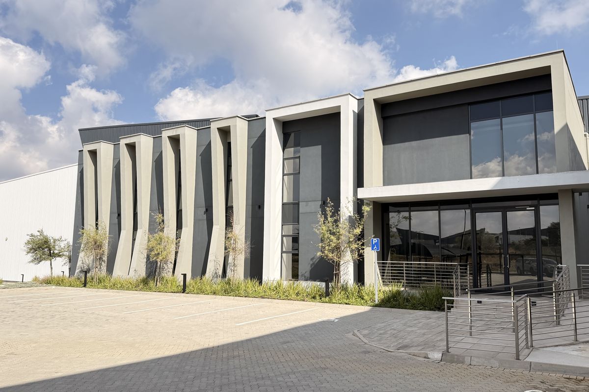 Modern industrial building facade featuring architectural fins, large glass windows, and a paved parking area with accessible ramp access.