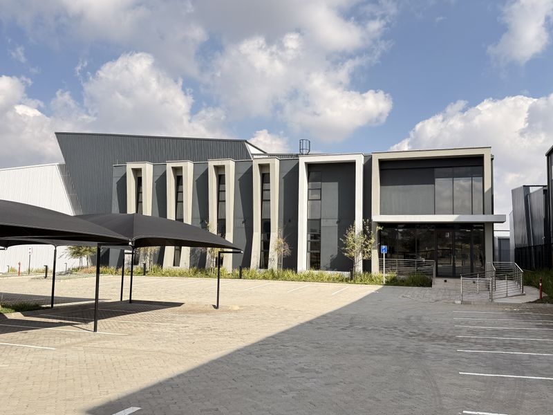Modern industrial office and warehouse facility featuring a paved parking area with shade cloth carports and a contemporary metal-clad facade.