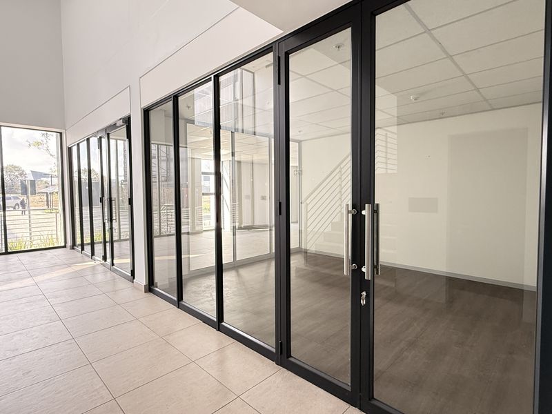 Modern industrial office space featuring extensive aluminium-framed glass partitioning, double glass doors, tiled flooring, and a clean, professional suspended ceiling finish.