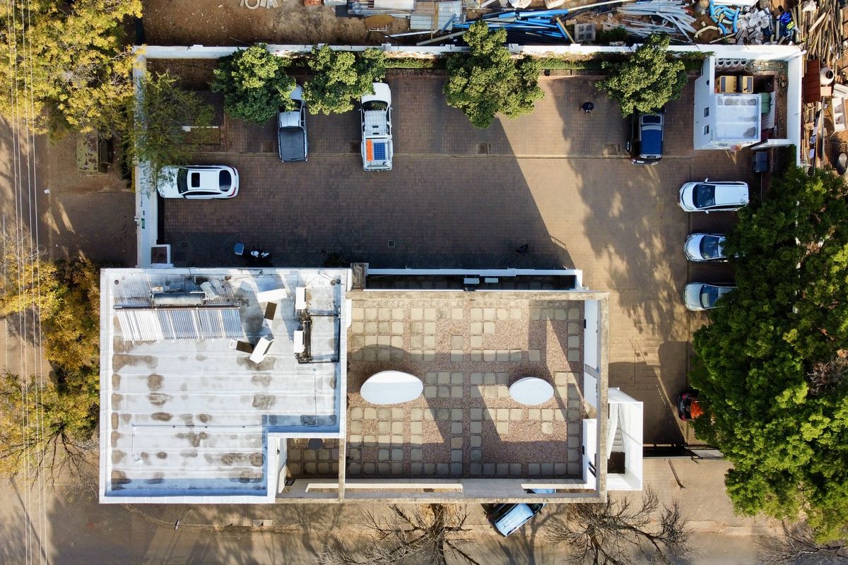 Aerial view of a commercial property featuring a paved parking lot, flat roof with solar heating, and a paved courtyard area.