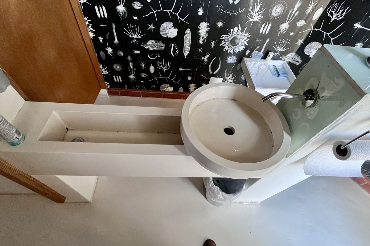 A modern bathroom featuring a unique custom-built concrete basin and wall-mounted faucet against a decorative patterned wall.