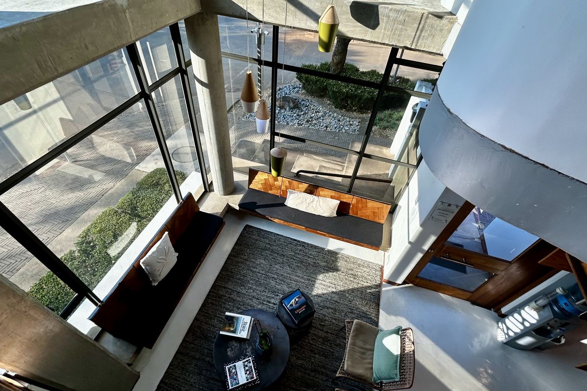 A bright, modern living area featuring floor-to-ceiling windows, exposed concrete structural elements, and built-in wooden bench seating with a contemporary architectural aesthetic.