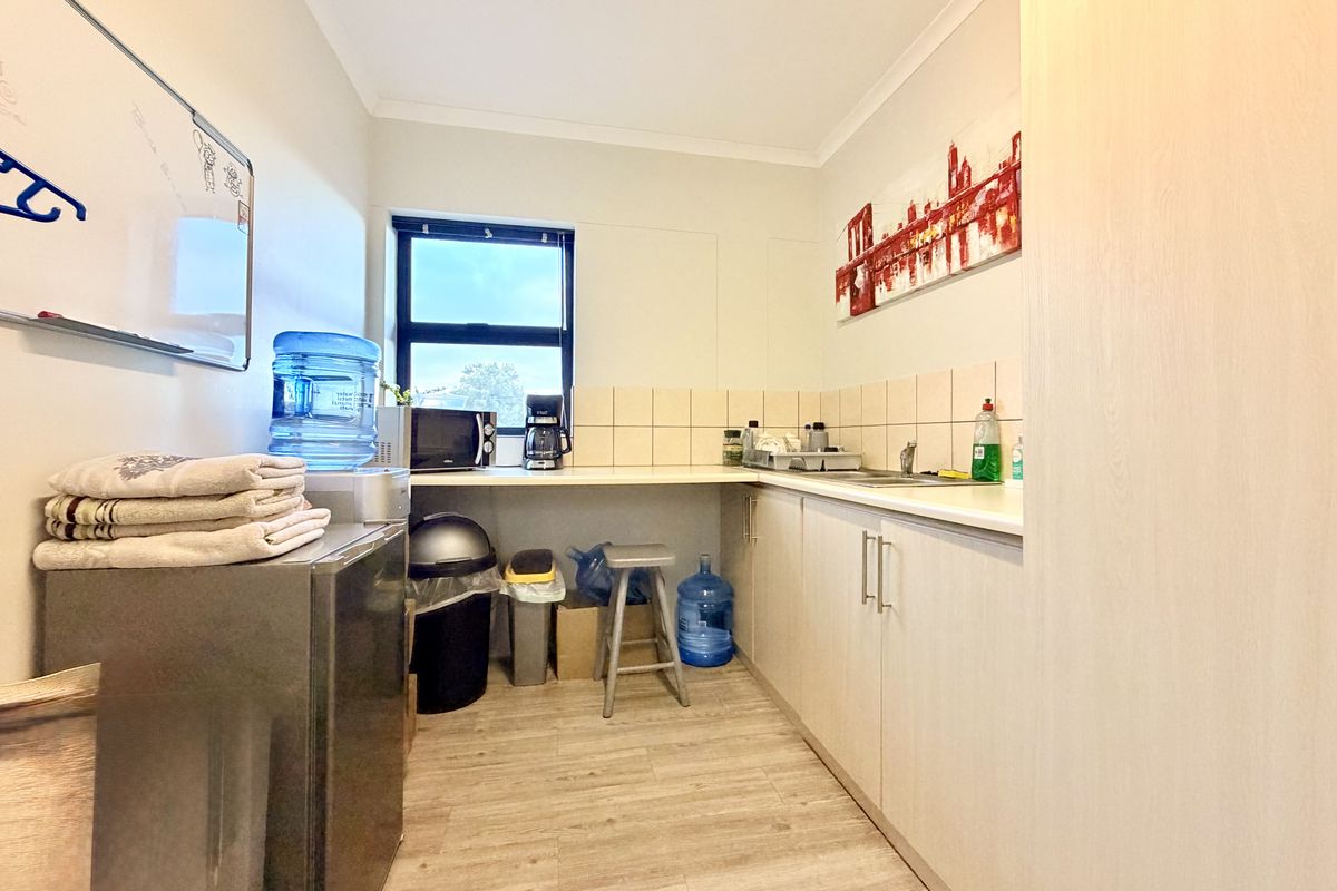 A functional kitchenette featuring laminate cabinetry, a tiled backsplash, and a stainless steel sink, providing essential utility space for a commercial office environment.