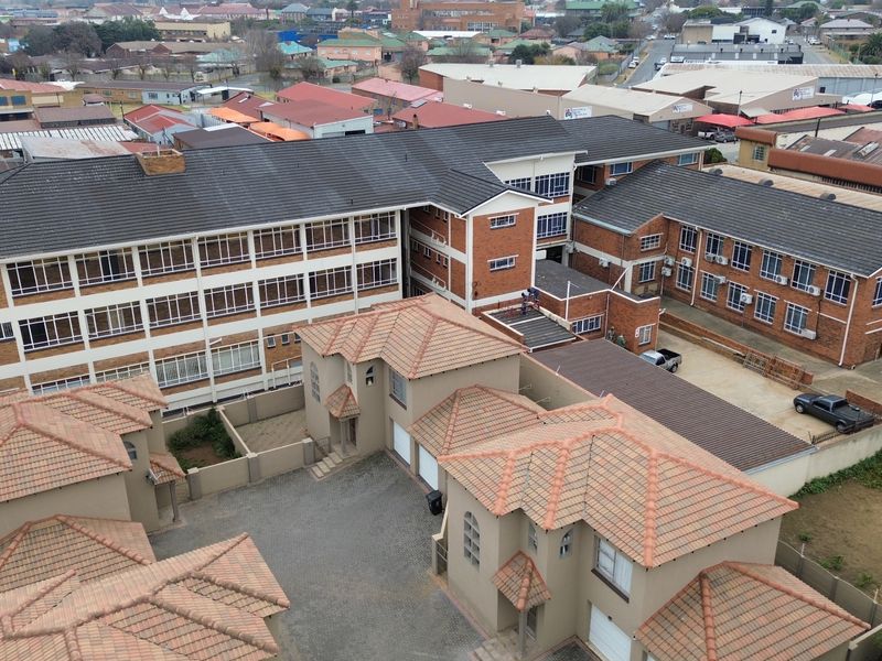 Aerial view of a multi-story office complex featuring brick construction, tiled roofing, and a paved courtyard area with integrated garage access.