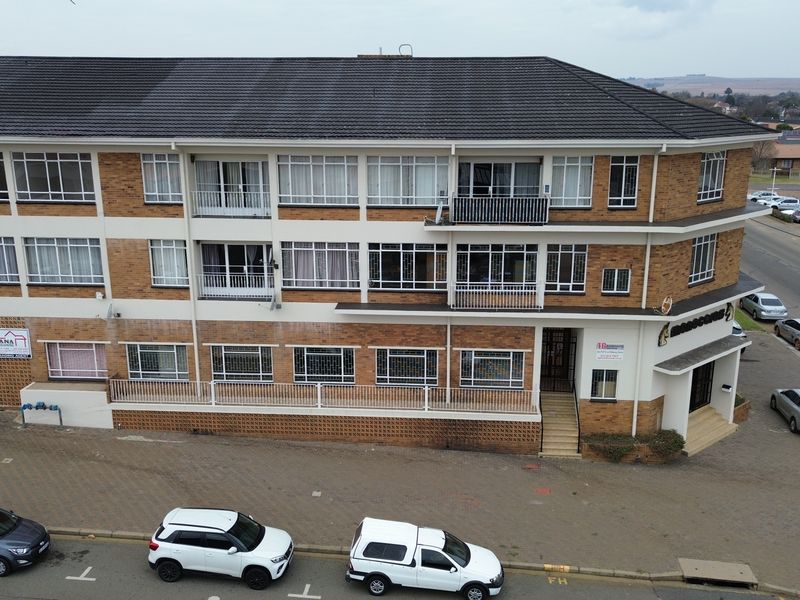 Aerial view of a multi-story brick office building featuring balconies, security window bars, and an adjacent paved parking area.