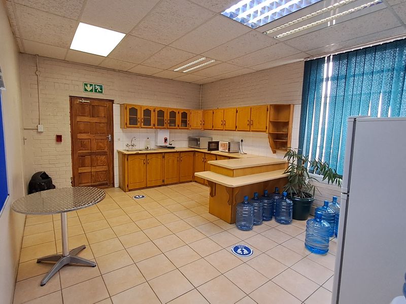 Office kitchen area featuring built-in wooden cabinetry, laminate countertops, a stainless steel sink, and tiled flooring with a drop ceiling.