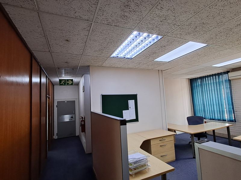 A functional office space featuring suspended ceilings, integrated fluorescent lighting, partition walls, and air conditioning, with vertical blinds providing natural light control.