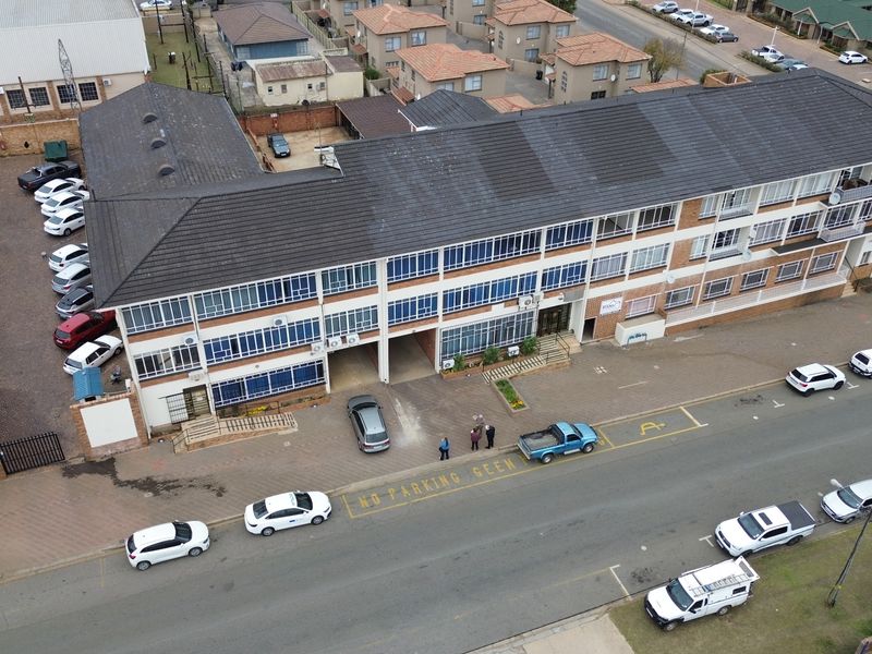 Aerial view of a multi-story office building featuring a tiled roof, external air conditioning units, and an adjacent paved parking area.