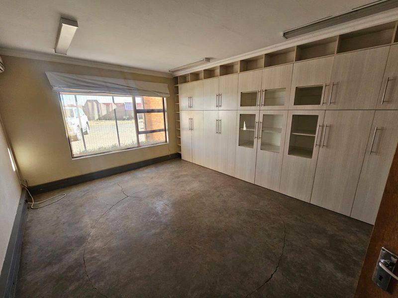 A functional office space featuring extensive built-in cabinetry, large windows for natural light, and durable concrete flooring.