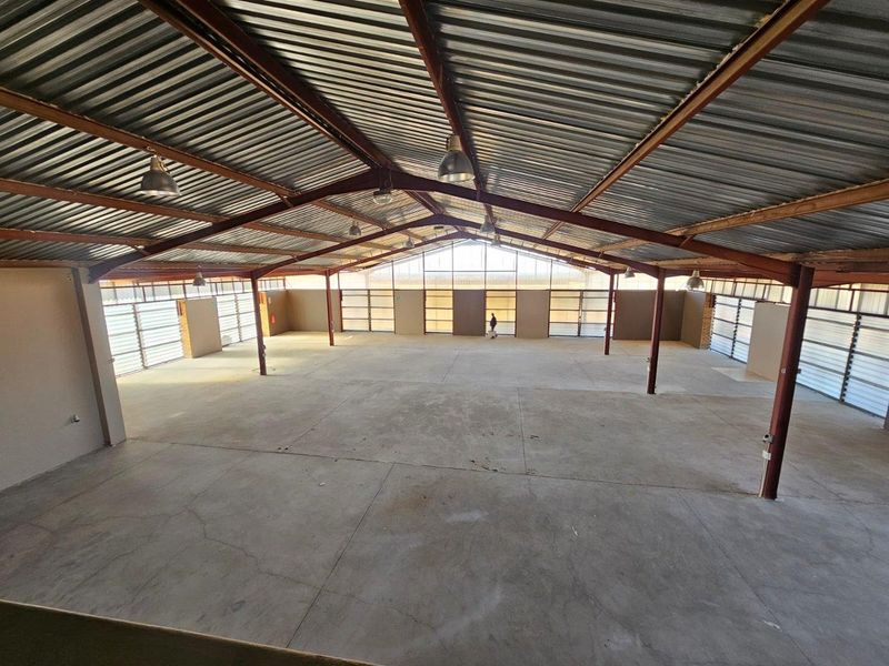 Spacious open-plan commercial warehouse area featuring high exposed steel trusses, concrete flooring, and abundant natural light through extensive louvre window installations.
