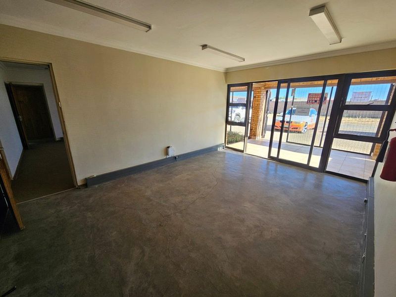 An empty commercial office space featuring concrete flooring, fluorescent lighting, and large sliding glass doors providing natural light and street access.