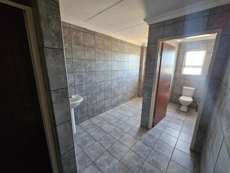 A clean, tiled bathroom featuring a pedestal washbasin and a separate toilet area with natural light.