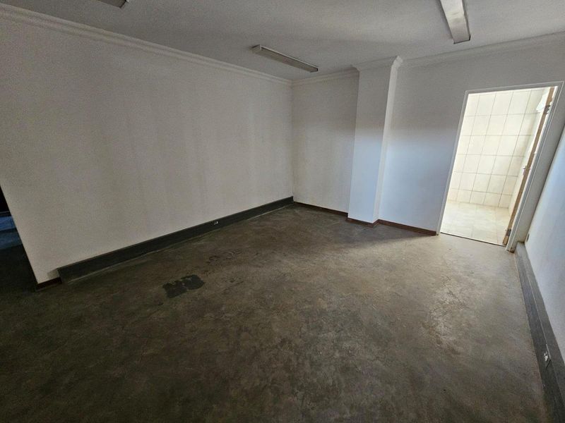 An empty commercial office space featuring concrete flooring, fluorescent lighting, and a doorway leading to an adjacent tiled area.