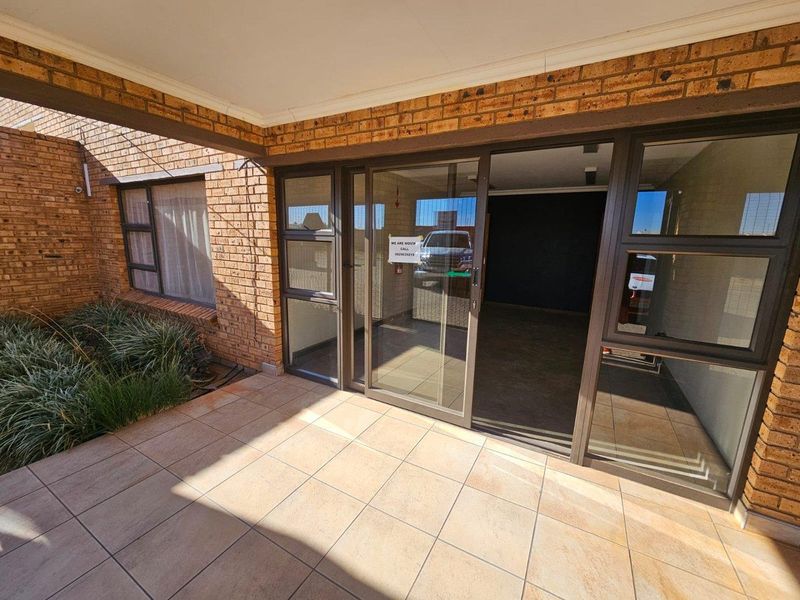 A covered patio area featuring tiled flooring and brick exterior walls, providing access to the interior through large sliding glass doors.