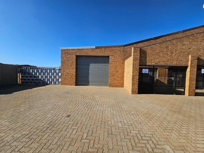 Commercial property exterior featuring a brick facade, a secure roller shutter door, and a spacious paved driveway area.