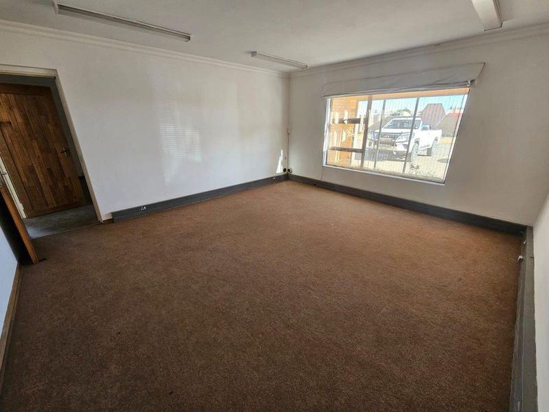 An empty, carpeted office space featuring large windows, fluorescent lighting, and a timber door, suitable for a professional workspace.