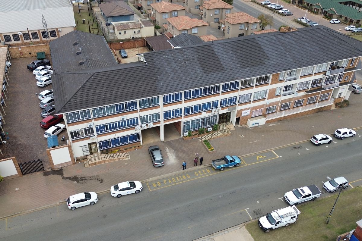 Aerial view of a multi-story office building featuring a tiled roof, external air conditioning units, and an adjacent paved parking area.