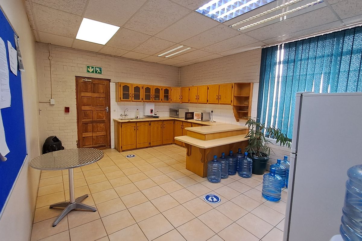 Office kitchen area featuring built-in wooden cabinetry, laminate countertops, a stainless steel sink, and tiled flooring with a drop ceiling.