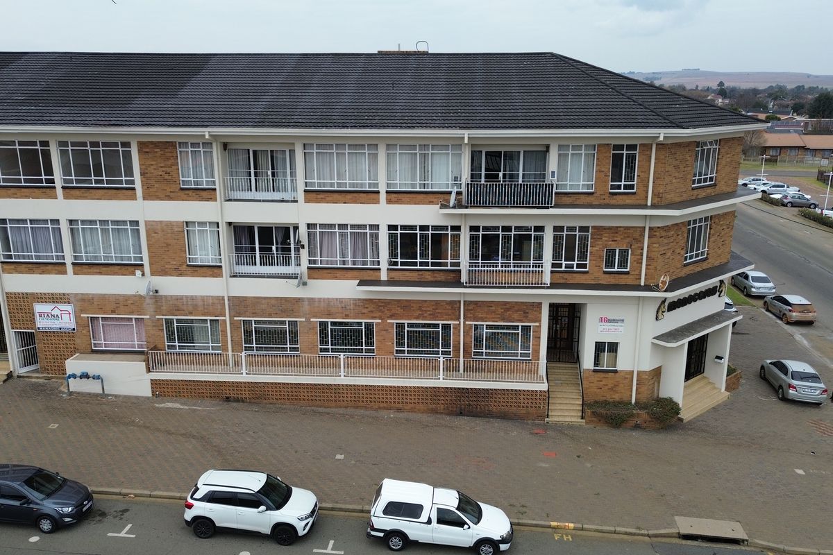 Aerial view of a multi-story brick office building featuring balconies, security window bars, and an adjacent paved parking area.