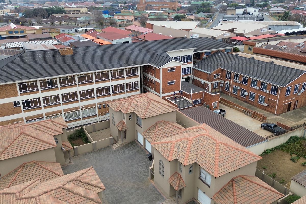 Aerial view of a multi-story office complex featuring brick construction, tiled roofing, and a paved courtyard area with integrated garage access.