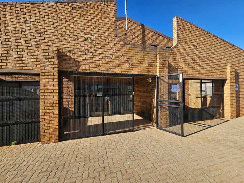Front entrance of a commercial property featuring a face brick facade, secure metal gate, and paved exterior area.