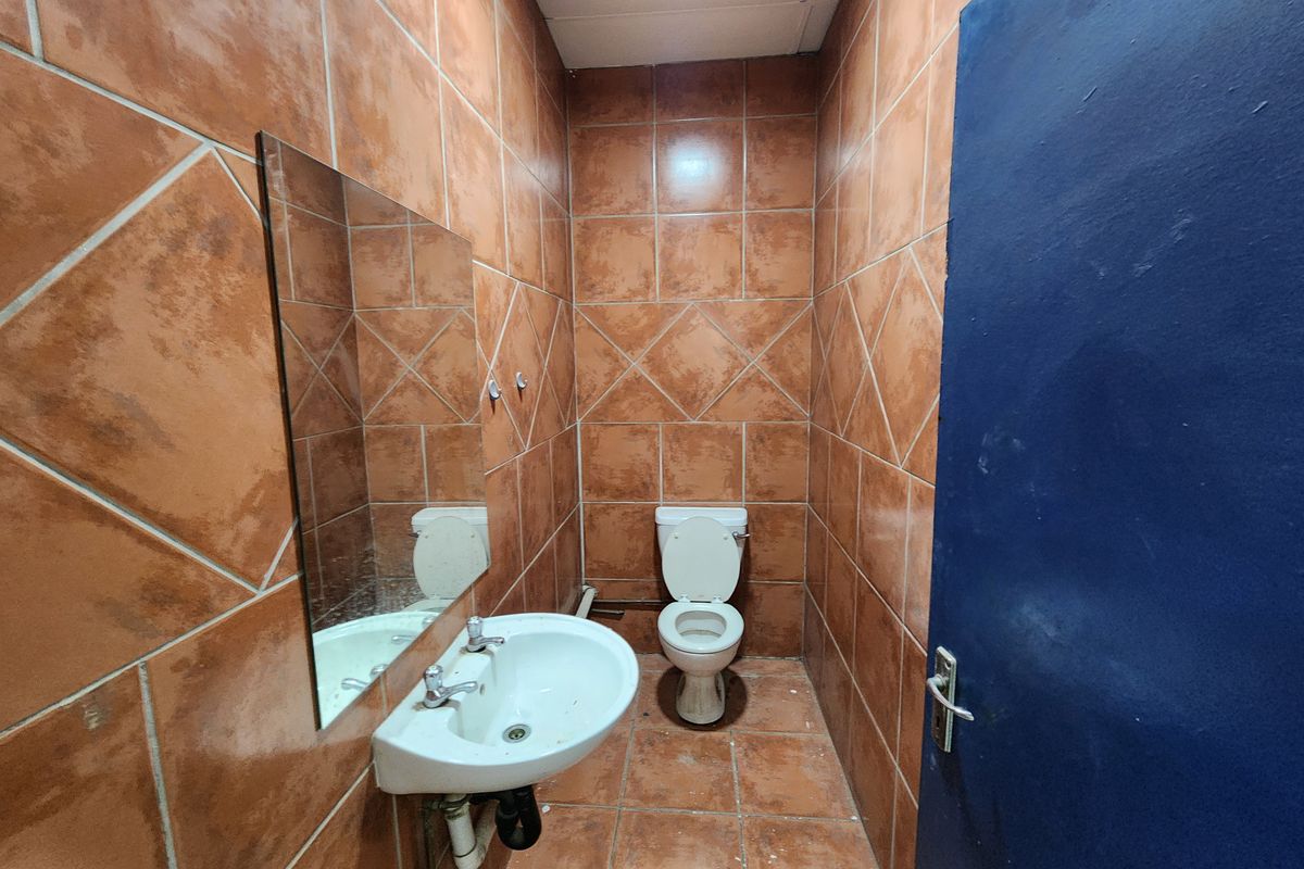 A compact industrial restroom featuring full-height terracotta-style wall tiling, a wall-mounted basin, and a standard toilet suite.