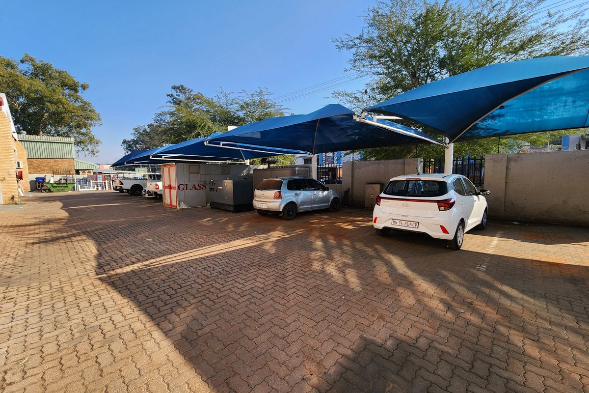 Outdoor parking area featuring paved ground surface and multiple blue shade net structures for vehicle protection.
