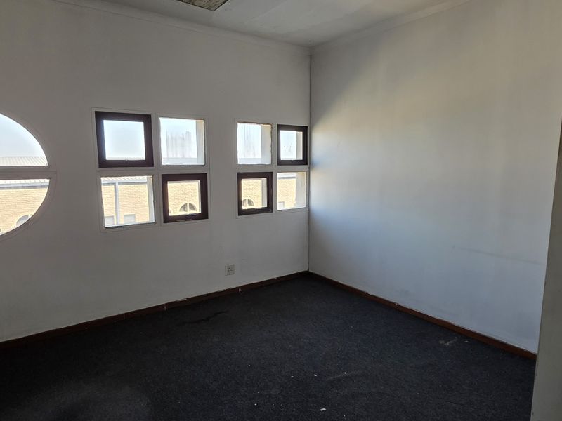 An empty office space featuring exposed brickwork, unique multi-pane windows, and carpeted flooring, suitable for a professional workspace or studio.
