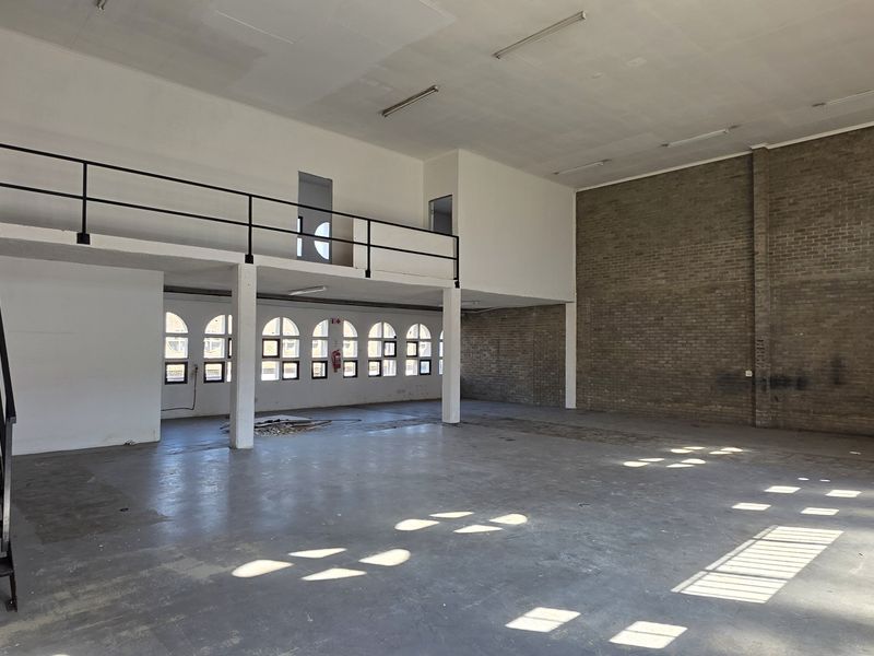 Spacious industrial utility area featuring a mezzanine level, metal staircase, exposed brick walls, and large arched windows providing ample natural light.