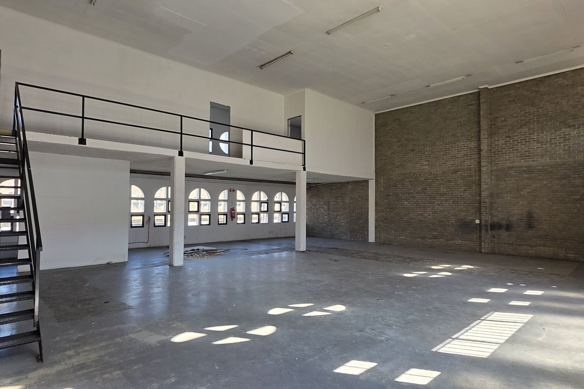 Spacious industrial utility area featuring a mezzanine level, metal staircase, exposed brick walls, and large arched windows providing ample natural light.