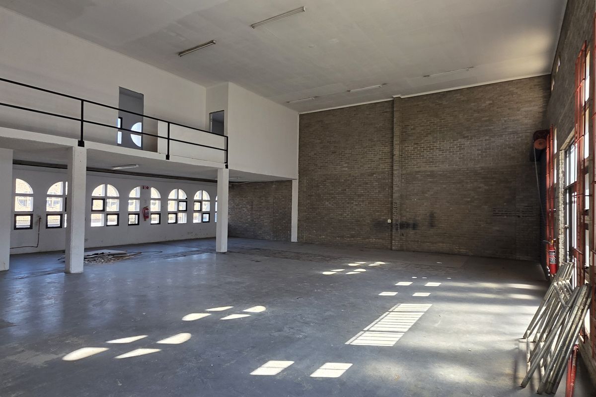 Spacious industrial open-plan area featuring a mezzanine level, exposed brick walls, large steel-framed windows, and durable concrete flooring.