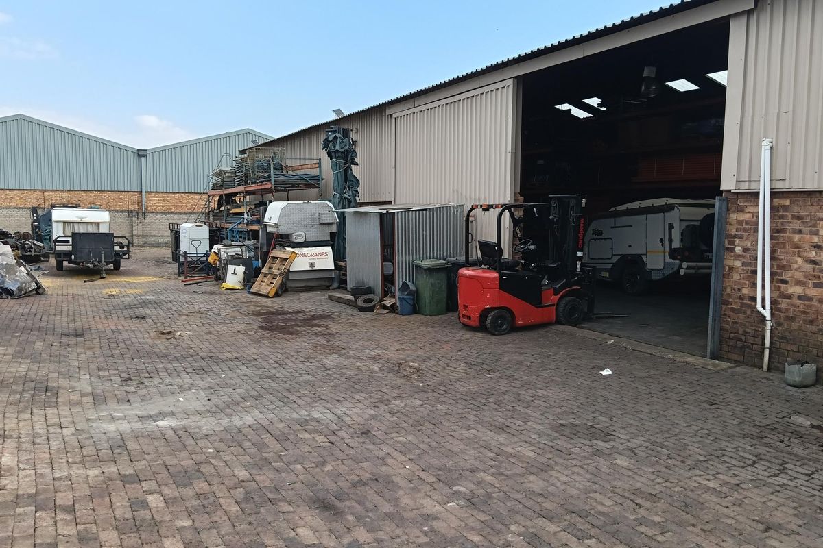 Industrial yard featuring a large warehouse structure with sliding doors, brick paving, and ample open storage space for operational equipment.