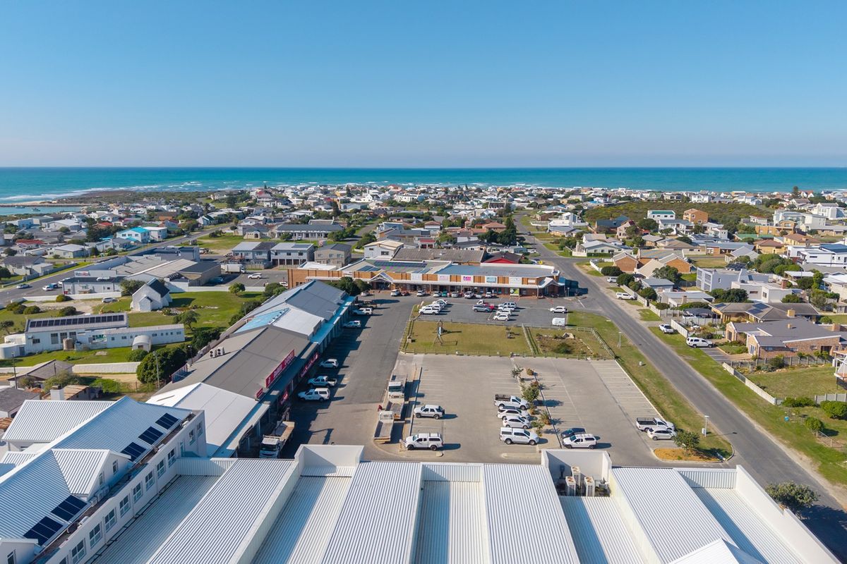 Aerial view of a commercial shopping complex featuring extensive parking facilities, metal roofing with solar panels, and surrounding coastal residential neighborhood.