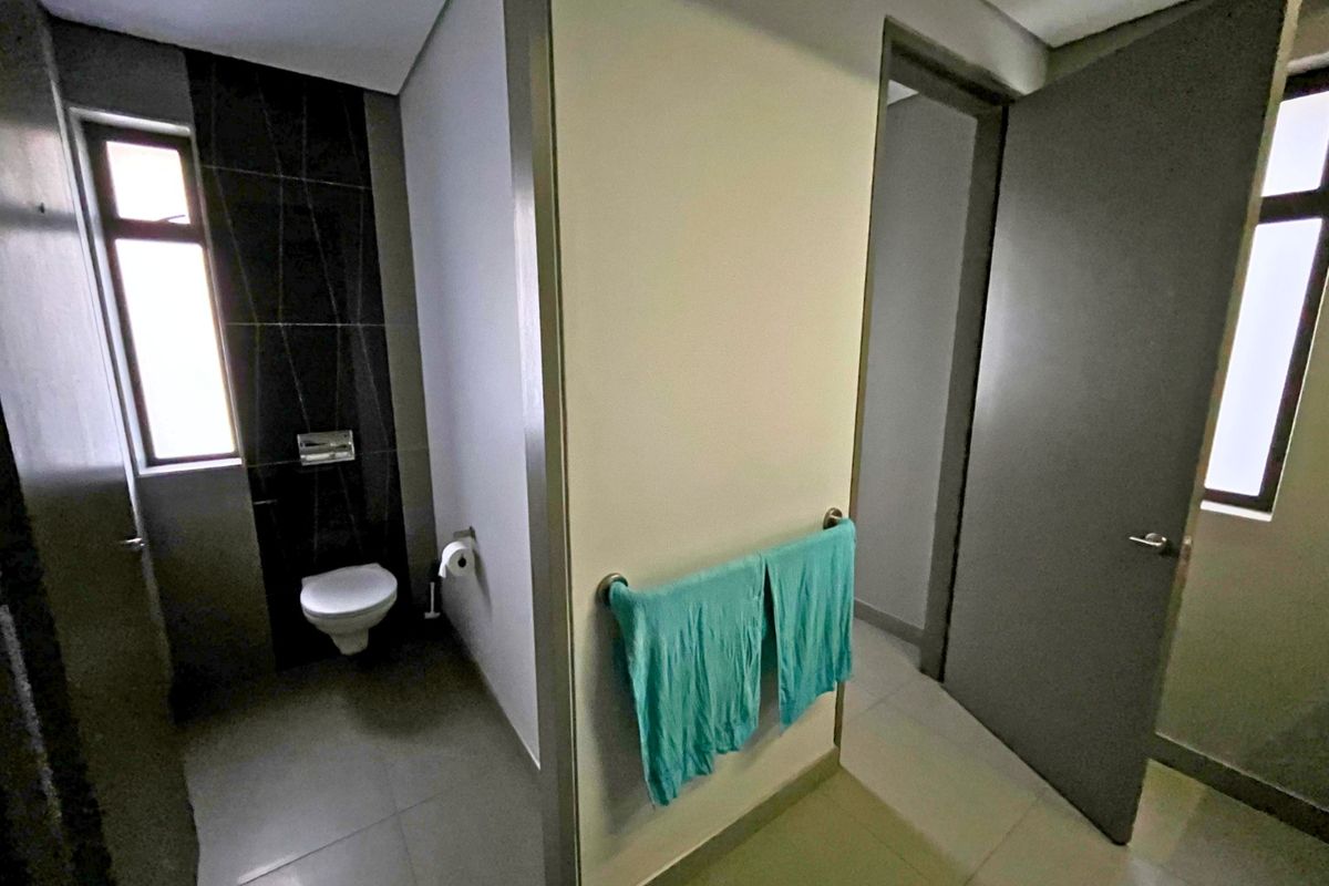 Modern office restroom featuring a wall-mounted toilet, tiled accent wall, and neutral floor finishes with a functional layout.