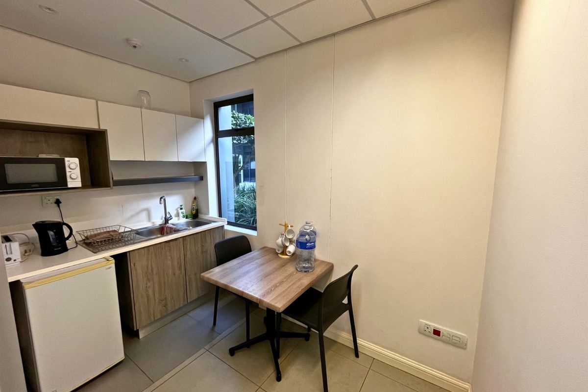A compact office kitchenette featuring built-in cabinetry, a stainless steel sink, and tiled flooring, providing a functional break area for staff.