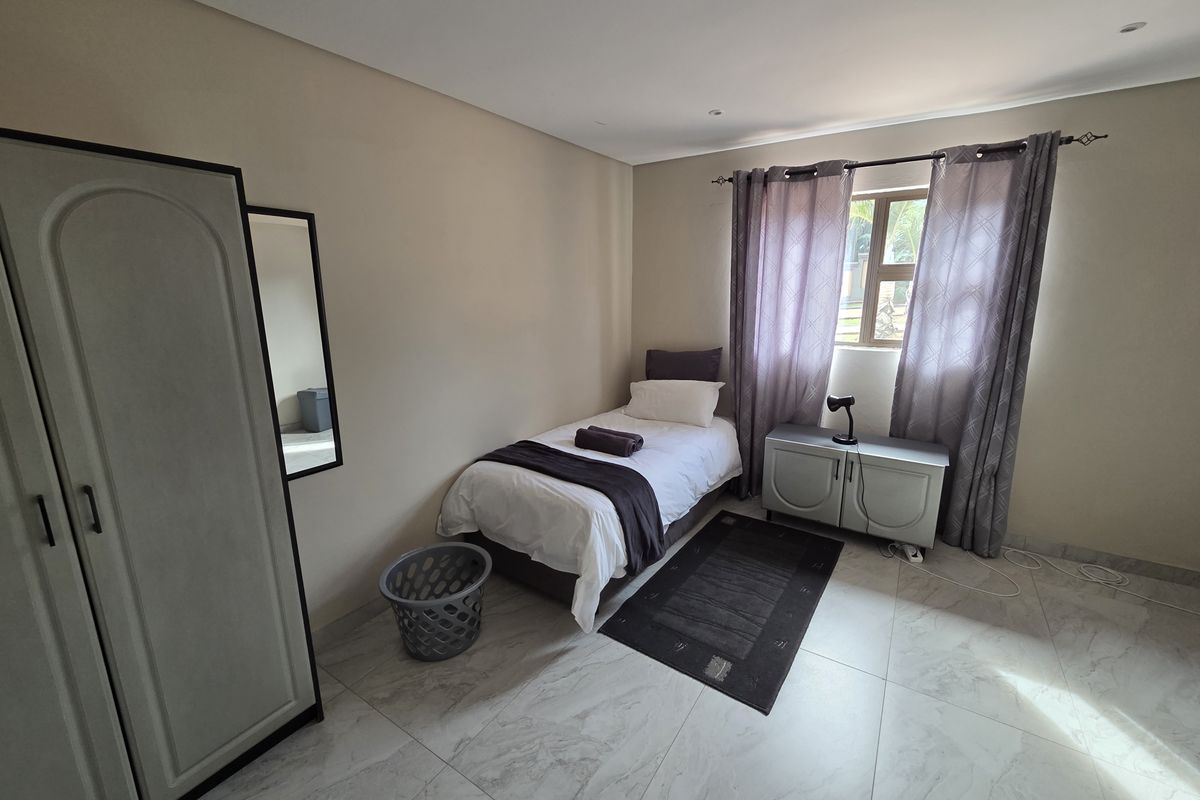 A bedroom featuring neutral wall tones, large format floor tiles, and recessed ceiling lighting, providing a clean and functional space.
