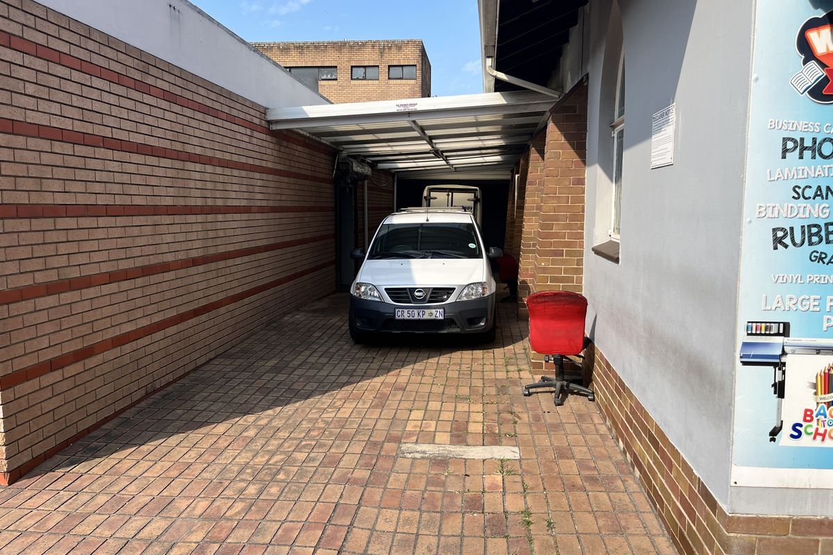 A covered outdoor parking or utility area featuring brick paving, brick walls, and a metal roof structure.