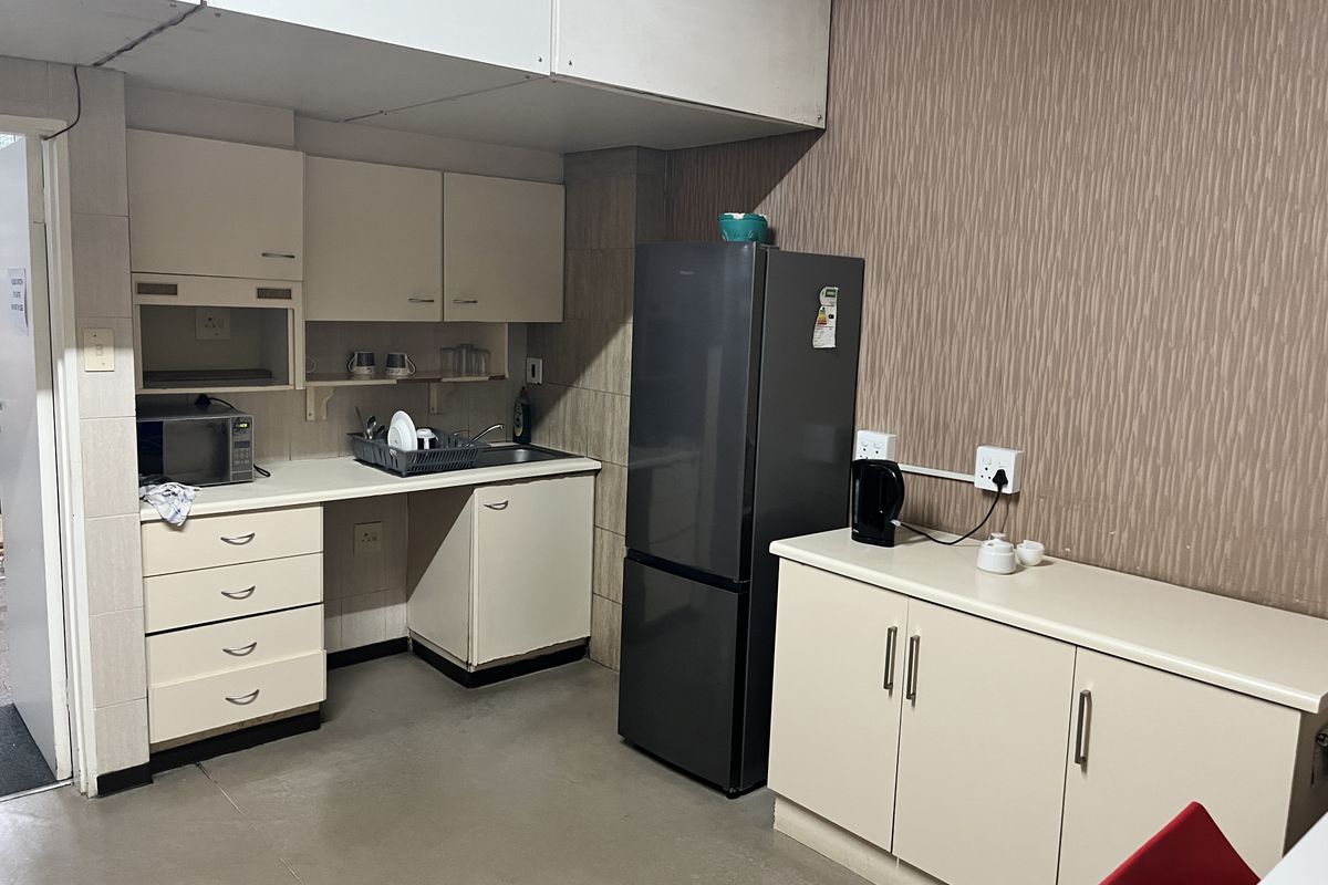 A functional commercial kitchenette featuring built-in cabinetry, a stainless steel sink, and dedicated space for a refrigerator and small appliances.