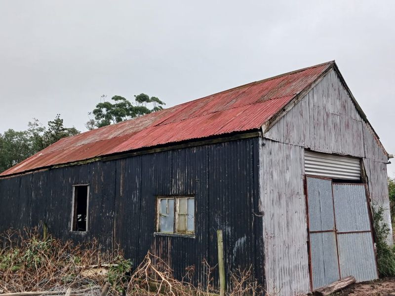 A weathered, detached utility shed or barn featuring corrugated metal construction, showing significant signs of age and exterior wear.