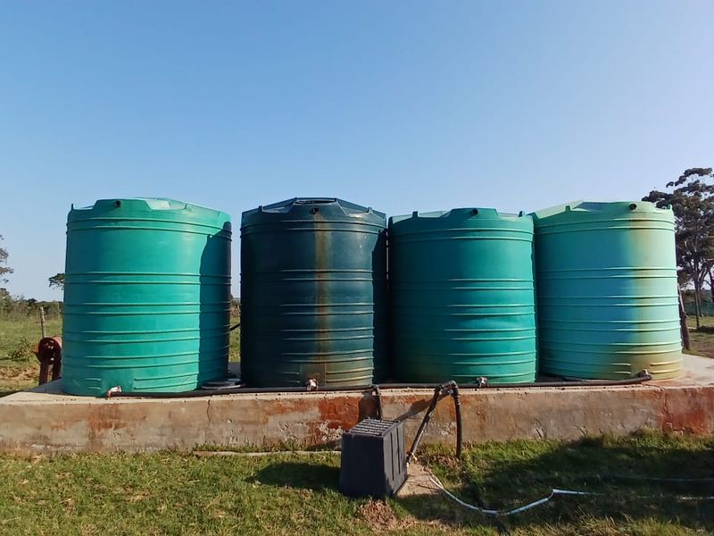 A set of four large plastic water storage tanks mounted on a raised concrete plinth, featuring integrated plumbing connections for farm water supply.
