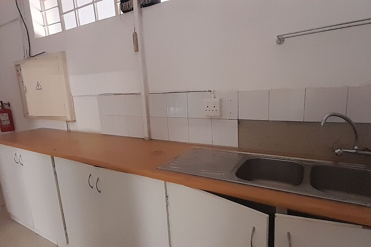 A functional office kitchenette featuring a double bowl sink, laminate countertops, and built-in cabinetry, currently in need of minor repairs and cosmetic updates.