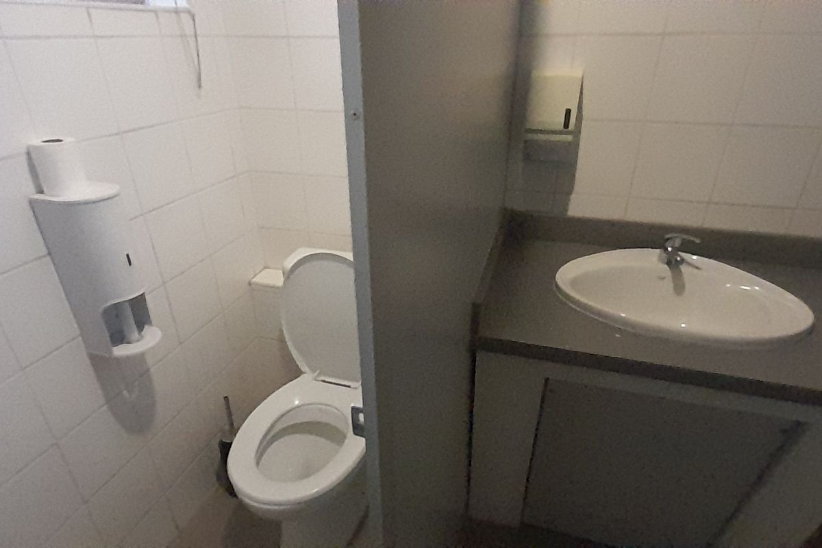 A functional office bathroom featuring a standard toilet, vanity basin with countertop, and tiled walls.